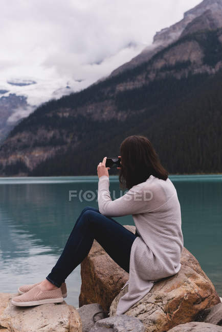Side view of woman clicking photos with camera near lakeside — Stock Photo