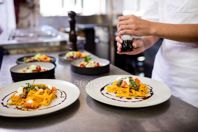 Sección media del chef usando molino de pimienta en la cocina del restaurante - foto de stock