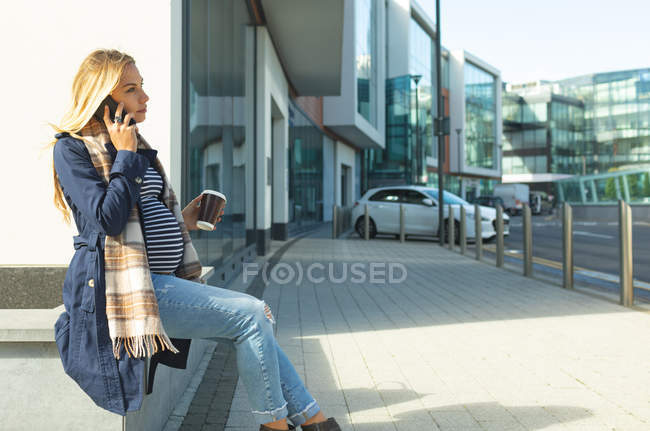 Вагітна жінка розмовляє по мобільному телефону в місті в сонячний день — стокове фото
