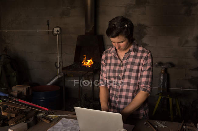 Metallschmiedin benutzt Laptop in Fabrik — Stockfoto