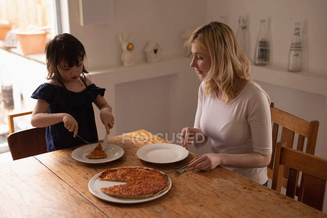 Madre e hija teniendo comida en la mesa de comedor en casa - foto de stock