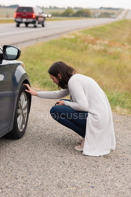 Вид збоку жінки, що перевіряє шини автомобіля під час поломки — стокове фото