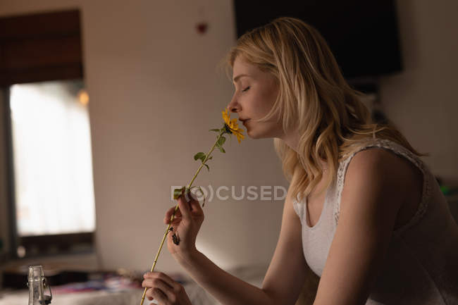 Hermosa mujer oliendo flor en casa - foto de stock