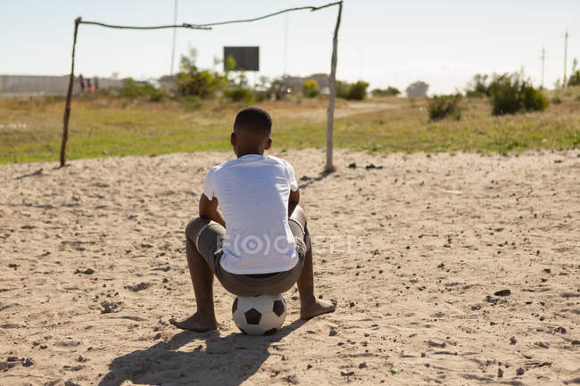 Вид ззаду хлопчика, що сидить на футболі в землі — стокове фото