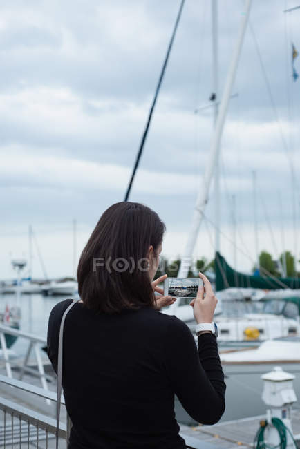 Vista posteriore della donna cliccando foto con il telefono cellulare vicino al porto — Foto stock