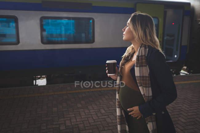 Pregnant woman having coffee on platform at railway station — Stock Photo