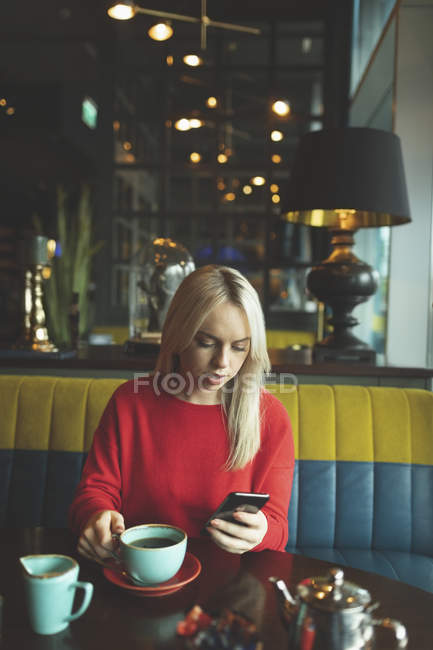 Женщина, пользующаяся мобильным телефоном во время кофе в кафе — стоковое фото