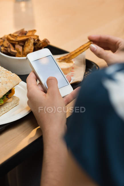Gros plan de la femme qui mange pendant qu'elle utilise son téléphone portable au restaurant — Photo de stock