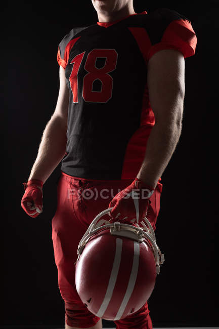 Mid section of American football player standing with helmet against black background — Stock Photo