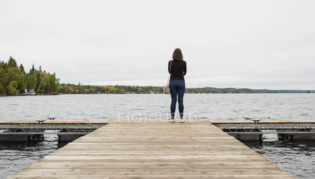 Вид ззаду жінки, що стоїть на причалі біля берега річки — стокове фото
