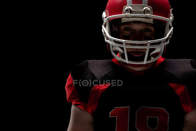 Американский футболист, стоящий в регби-шлеме на черном фоне — стоковое фото