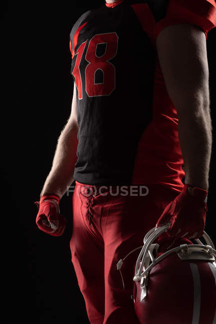 Seção média do jogador de futebol americano de pé com capacete contra fundo preto — Fotografia de Stock