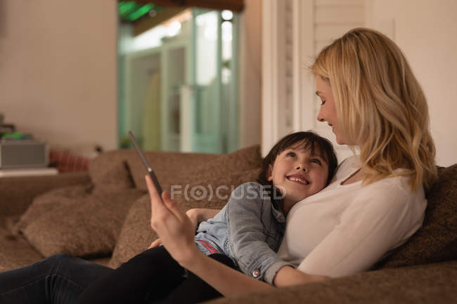 Mother and daughter using digital tablet in living room at home — Stock Photo