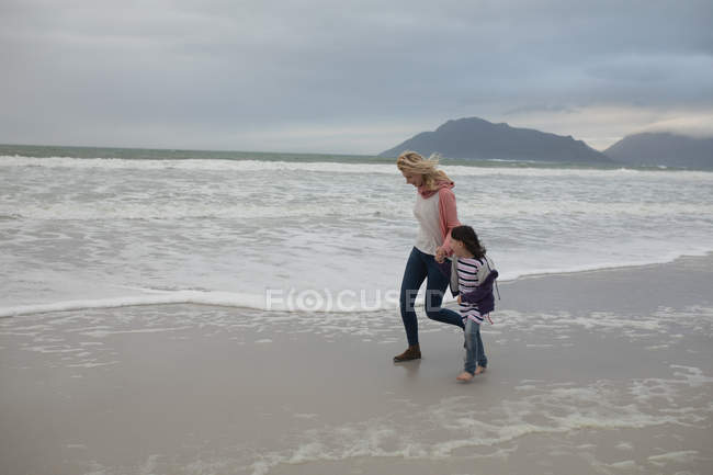 Madre e hija caminando juntas de la mano en la playa - foto de stock