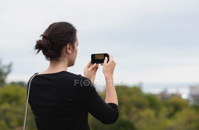 Вид ззаду жінки, що клацає фотографіями з мобільним телефоном — стокове фото