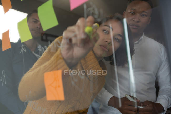 Женщина-руководитель пишет на стеклянной стене в офисе — стоковое фото