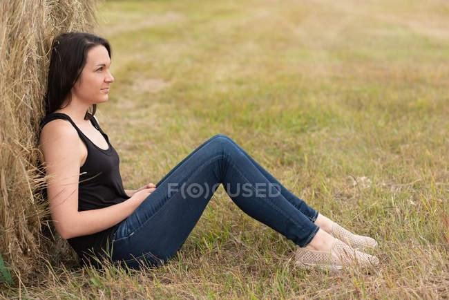 Donna premurosa rilassante contro balla di fieno nel campo — Foto stock