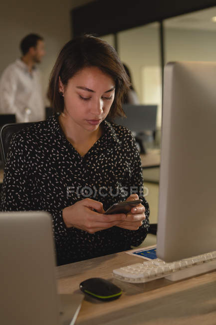 Жіночий керівник використовує мобільний телефон за столом в офісі — стокове фото