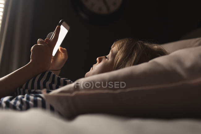 Femme utilisant un téléphone portable sur le lit dans la chambre à coucher à la maison — Photo de stock