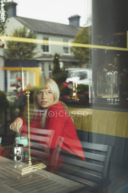 Femme regardant par la fenêtre tout en remuant le café dans le café — Photo de stock