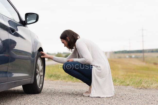 Vue latérale de la femme vérifiant le pneu de voiture pendant la panne — Photo de stock