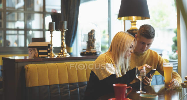 Молодая пара обсуждает по мобильному телефону в ресторане — стоковое фото