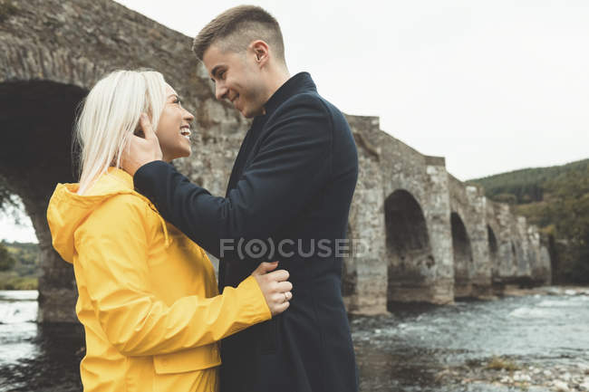 Felice giovane coppia abbracciando vicino al fiume — Foto stock