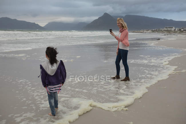 Щаслива мати натискає фотографію своєї дочки на пляжі — стокове фото