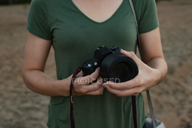Partie médiane de la femme tenant la caméra sur la plage — Photo de stock