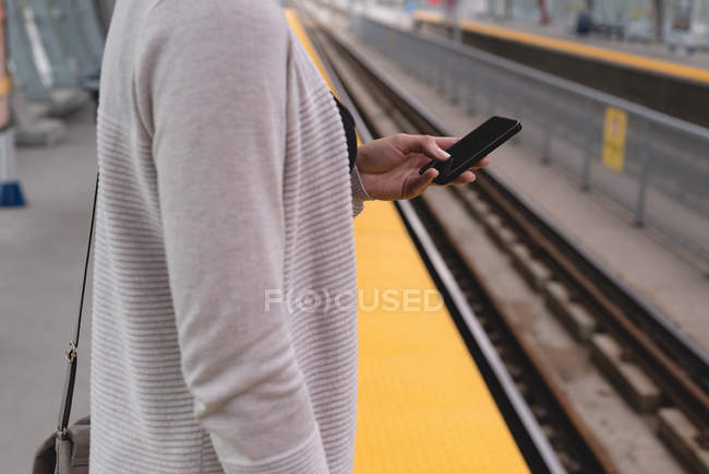 Vista lateral de la mujer utilizando el teléfono móvil en la plataforma en la estación de tren - foto de stock