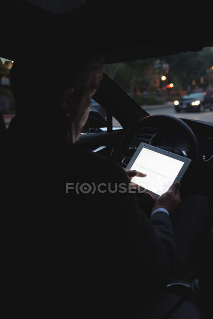 Задний план бизнесмена, использующего цифровой планшет в автомобиле — стоковое фото
