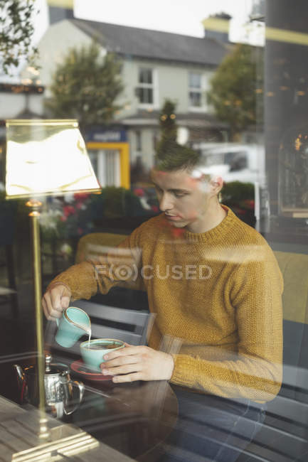 Young man pouring milk in coffee cup at cafeteria — Stock Photo