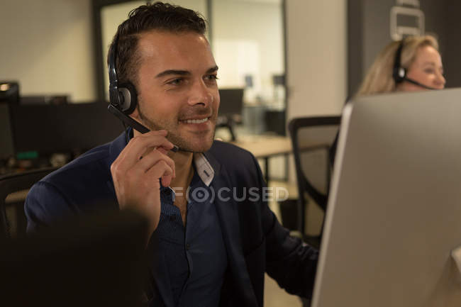 Executivo de atendimento ao cliente falando sobre fone de ouvido na mesa no escritório — Fotografia de Stock