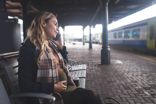 Vista laterale della donna incinta che parla al telefono cellulare alla stazione ferroviaria — Foto stock