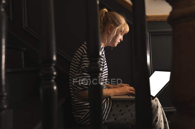 Vista lateral da mulher usando laptop nas escadas em casa — Fotografia de Stock