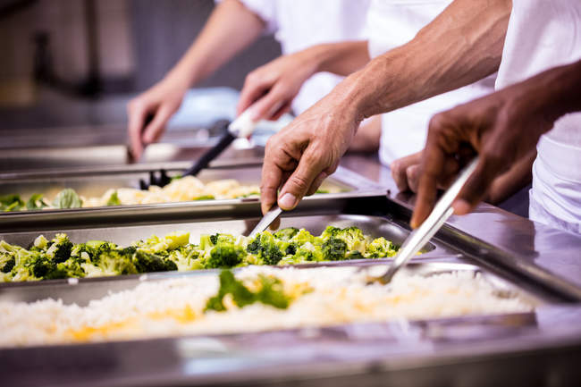 Section moyenne de chefs debout au plateau de service de la nourriture dans la cuisine — Photo de stock