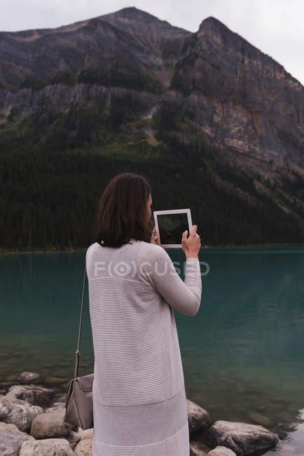 Visão traseira da mulher clicando fotos com tablet digital perto do lago — Fotografia de Stock