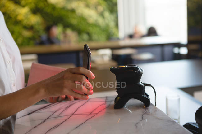 Mid section of woman paying with mobile phone through NFC technology at cash counter — Stock Photo