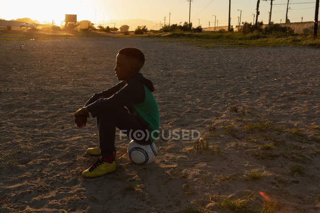 Menino sentado no futebol no chão ao entardecer — Fotografia de Stock