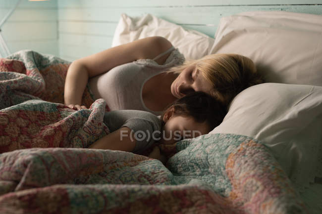 Madre e hija durmiendo en el dormitorio en casa - foto de stock