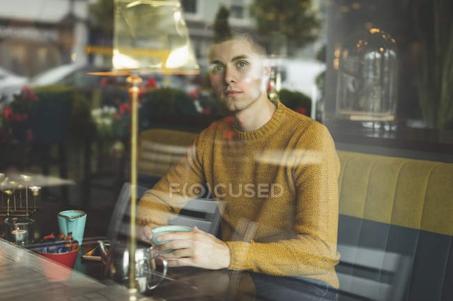 Чоловік дивиться крізь вікно, маючи каву в кафе — стокове фото