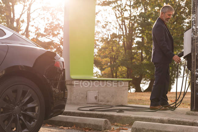 Businessman holding plug of charger at charging station on a sunny day — Stock Photo