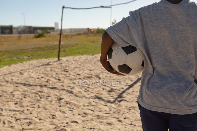 Вид сзади мальчика, держащего футбол в земле — стоковое фото