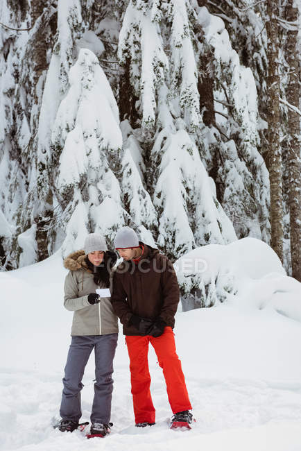 Pareja con tarjeta de dirección de pie en el paisaje nevado - foto de stock