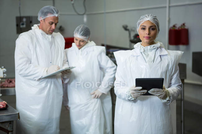 Женщина-техник держит планшет с коллегами на мясокомбинате — стоковое фото