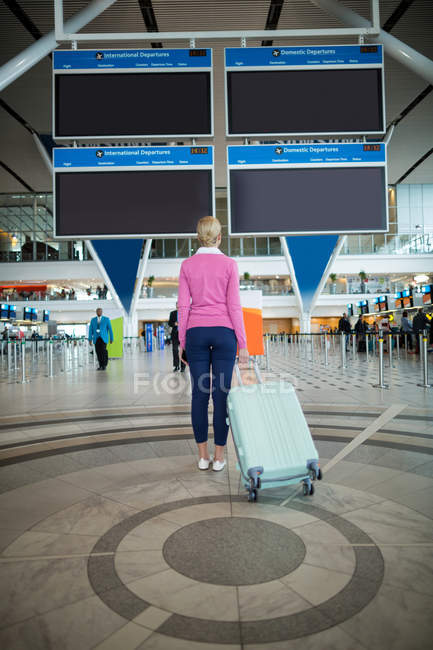 Vista traseira do viajante feminino em pé com bagagem na área de espera no aeroporto — Fotografia de Stock