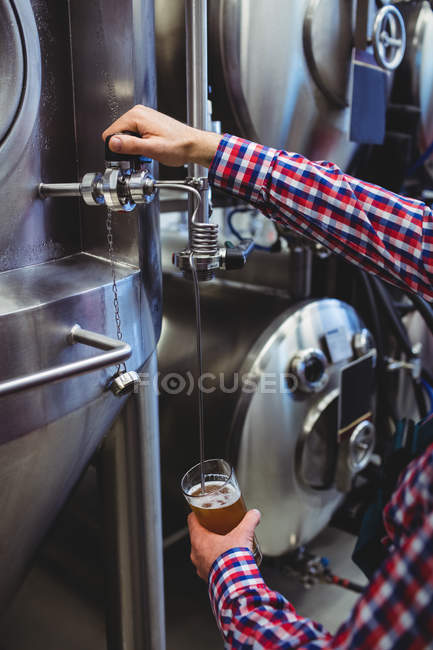 Midsection of manufacturer filling beer into glass from storage tank at distillery — Stock Photo