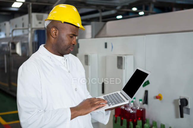 Trabajador masculino serio usando el ordenador portátil en la fábrica del jugo - foto de stock
