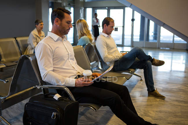 Des hommes d'affaires lisent un journal dans la salle d'attente du terminal de l'aéroport — Photo de stock
