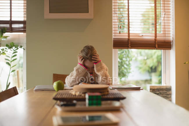Chica frustrada sentada en la mesa y estudiando en la sala de estar en casa - foto de stock